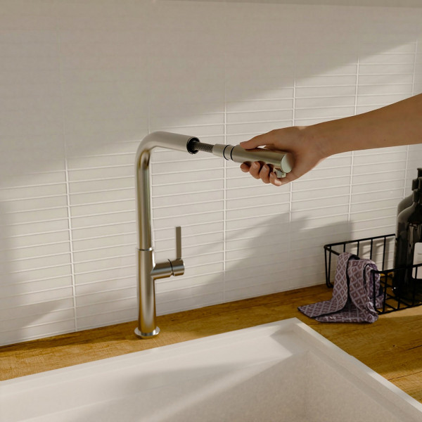 Hand zieht ausziehbaren Brausekopf aus einem Metall-Wasserhahn über einer Spüle.