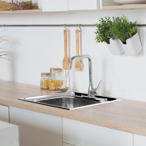 Edelstahlspüle mit Armatur in heller Küchenarbeitsplatte, im Hintergrund Küchenutensilien und Pflanzen.