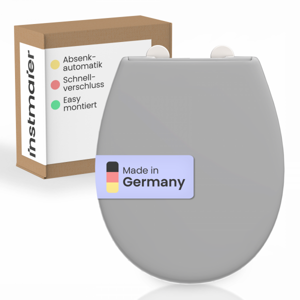 Grauer WC-Sitz mit Aufkleber „Made in Germany“ vor Karton mit Produktmerkmalen.