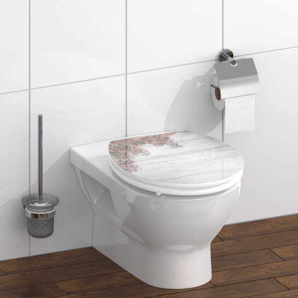 Wandhängende weiße Toilette mit WC-Deckel in Holzoptik und Blumenmotiv, daneben Toilettenbürste und Papierhalter.