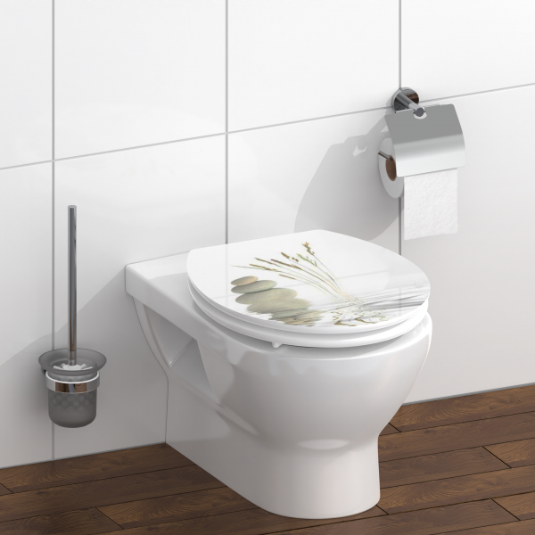 Wandhängende Toilette mit geschlossenem Deckel und Naturmotiv, daneben Bürste und Papierhalter.
